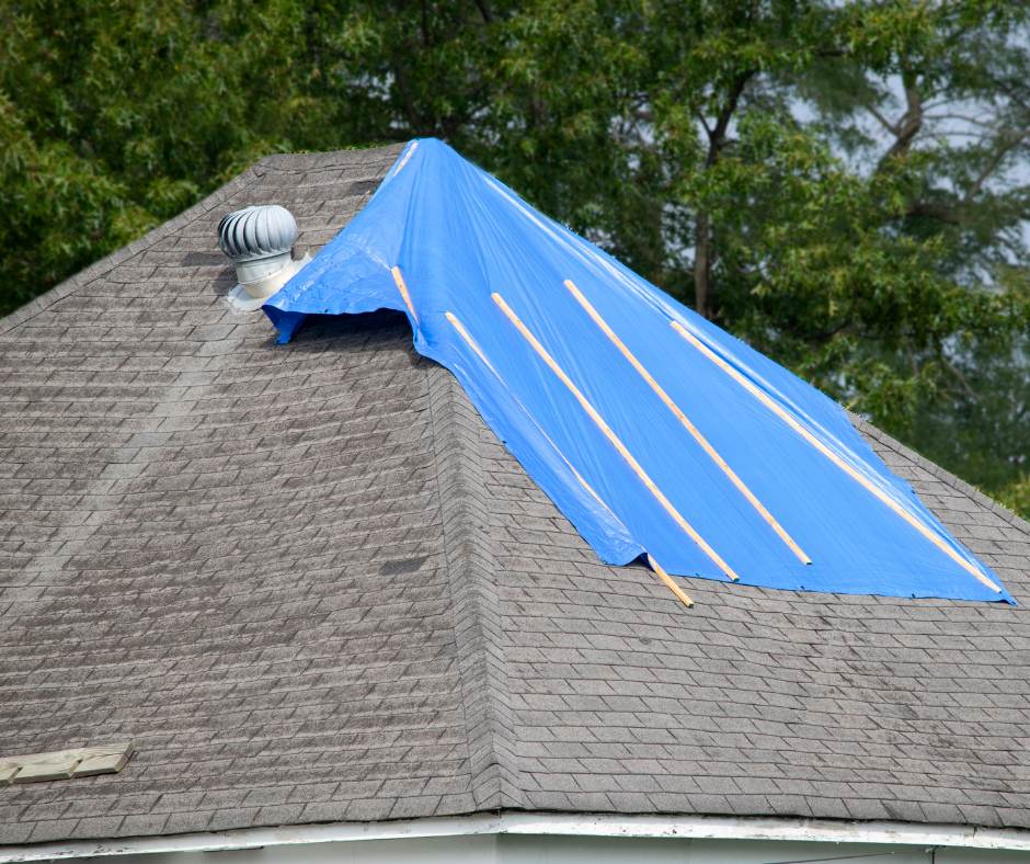 A roof with damage shingles that are covered by a blue tarp